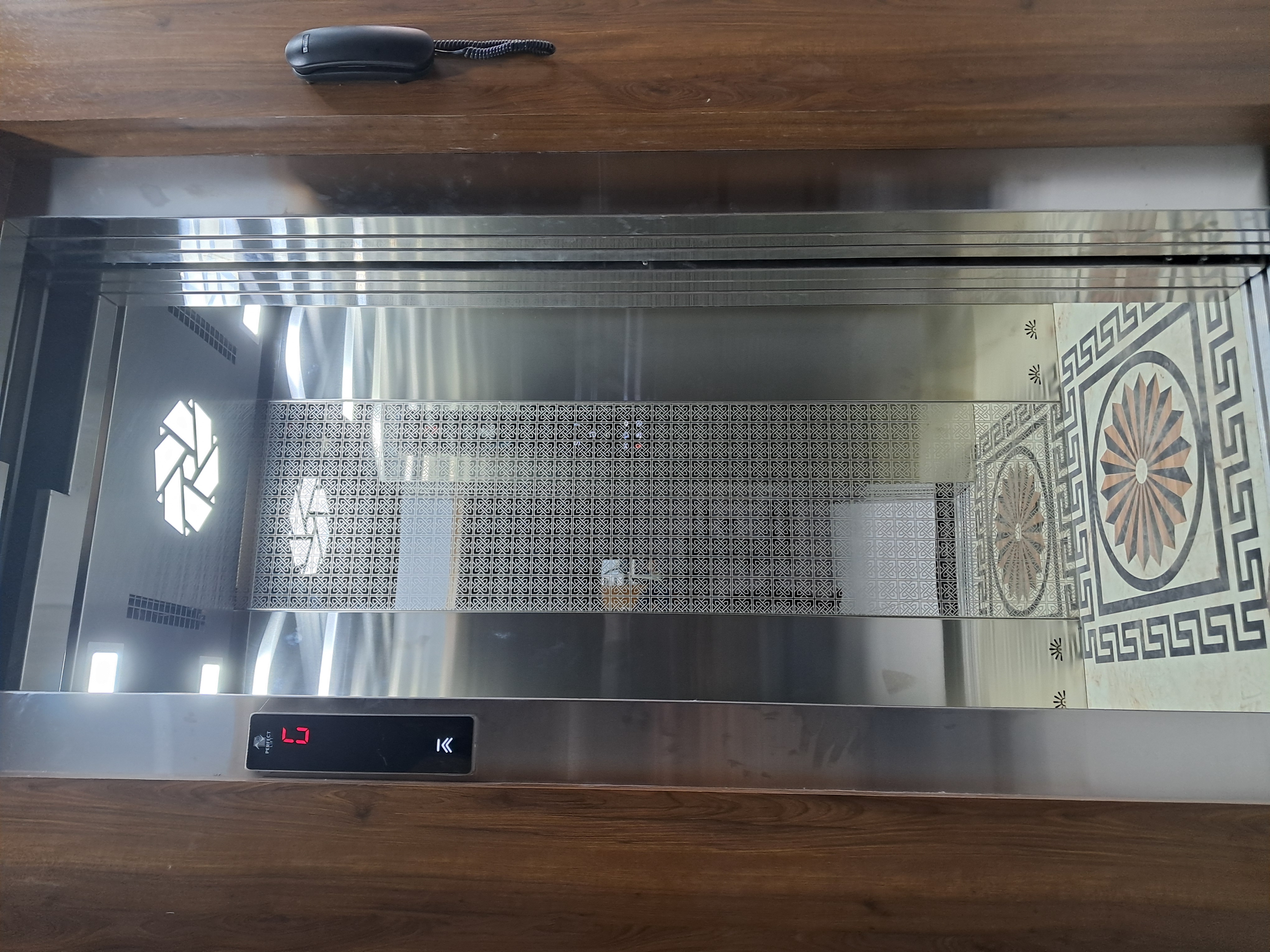 Elevator with wooden frame, stainless steel interior, and decorative floor pattern
